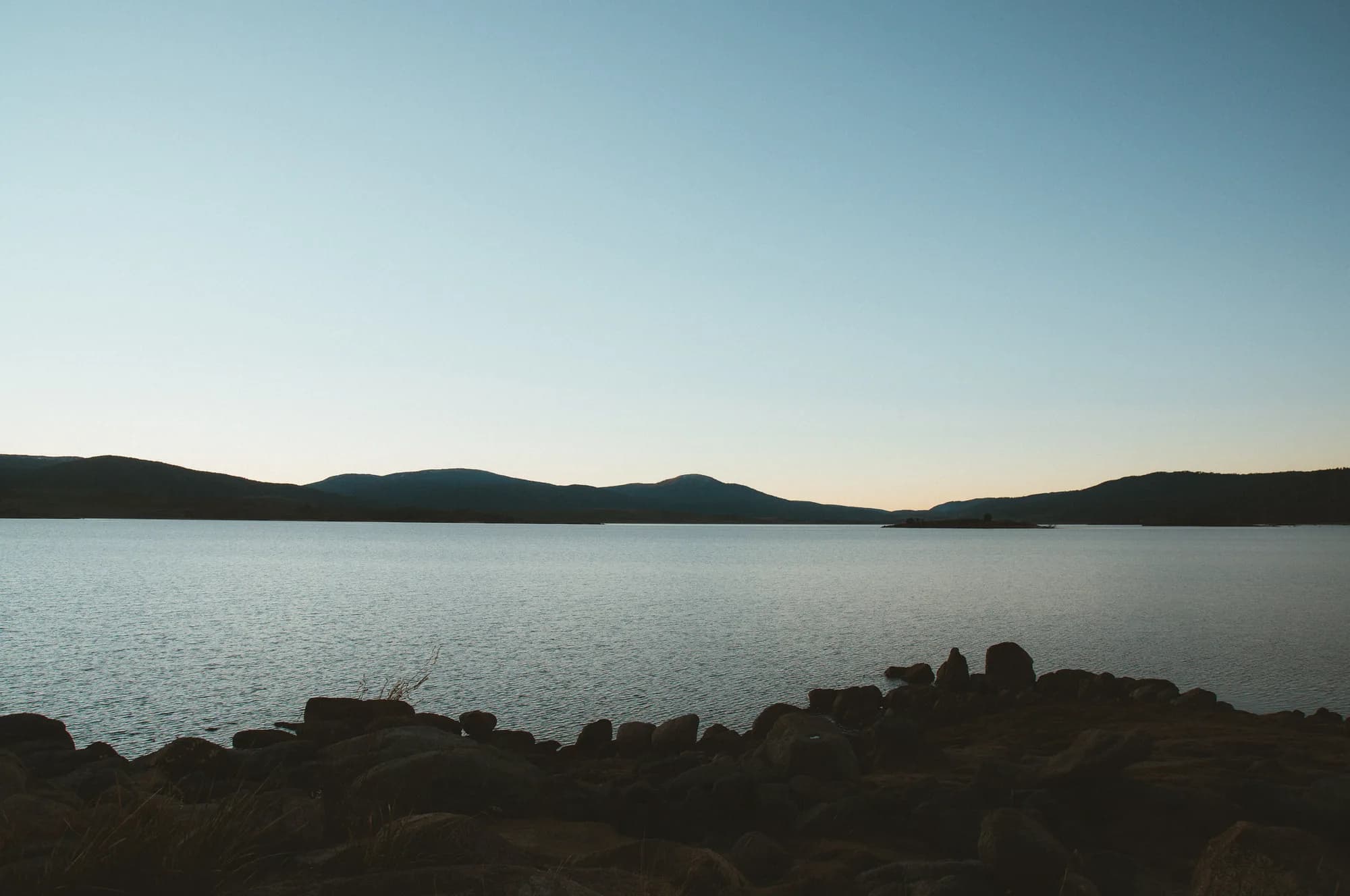 A calm Australian lake at dusk with mountains silhouetted on the horizon