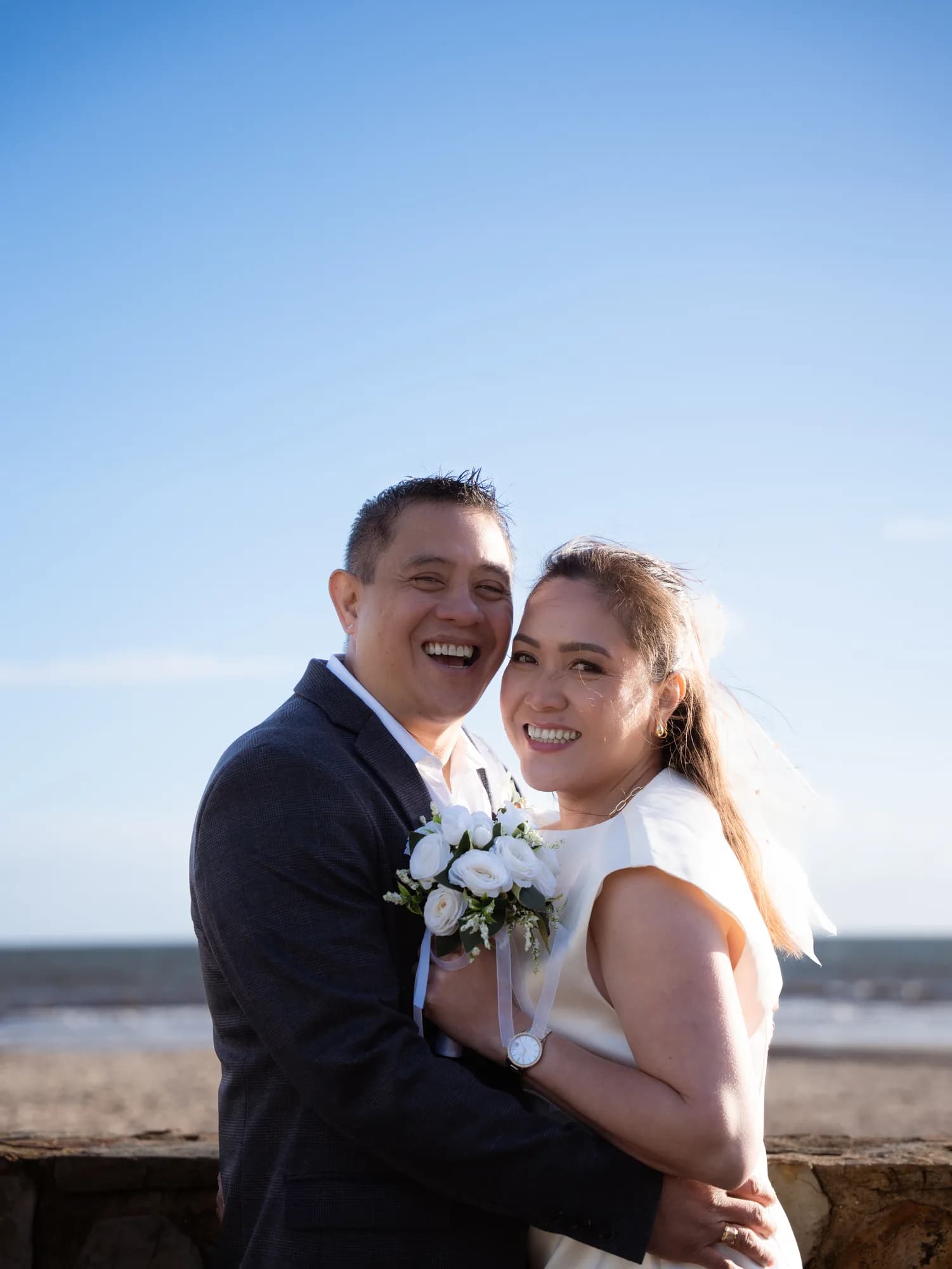 A newlywed couple laughing together by the beach