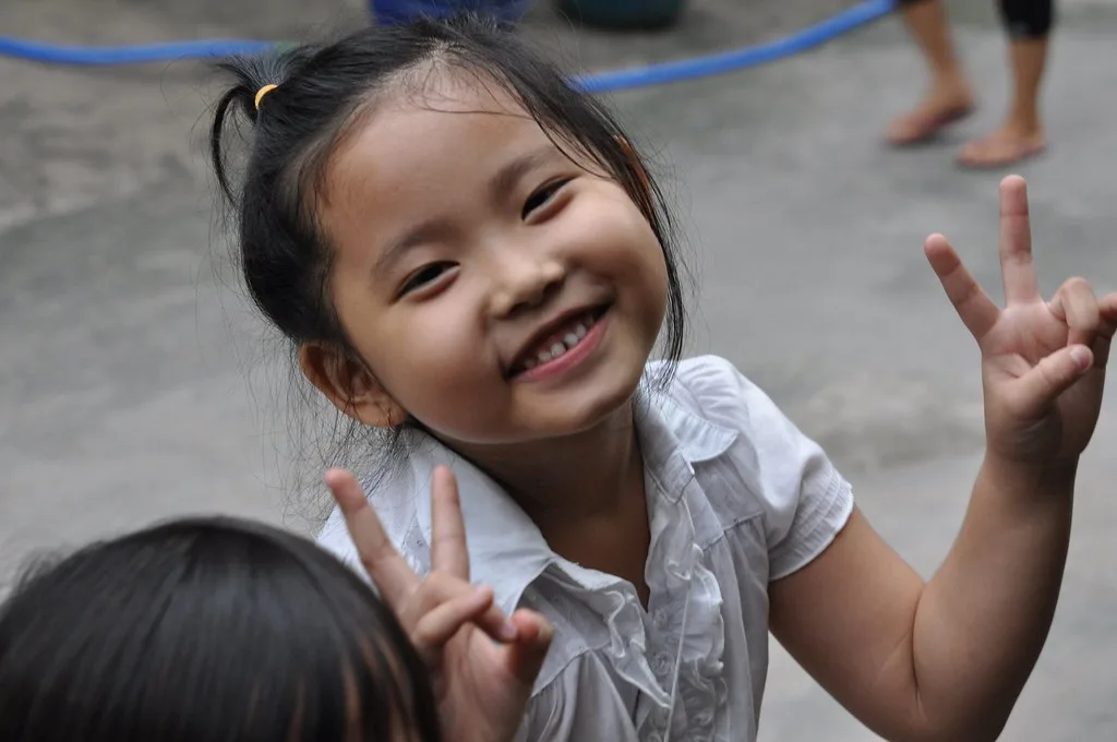 A young girl in Vietnam smiling and making a peace sign at the camera
